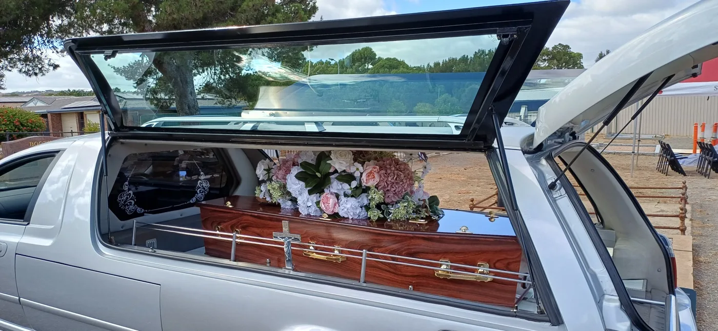 Signature Funeral Services hearse carrying a timber coffin with a floral spray